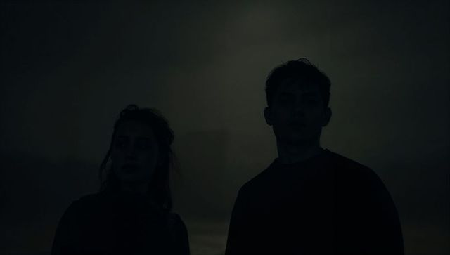 Silhouetted duo standing in foggy twilight with backlight halo, moody cinematic portrait