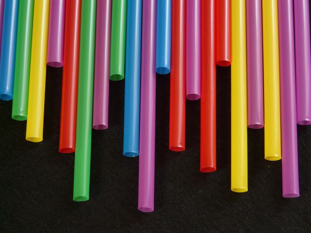 Colorful plastic drinking straws in vibrant colors hanging vertically against a black background. Can be used for eco-friendly awareness campaigns, party-themed promotions, or artistic representations.