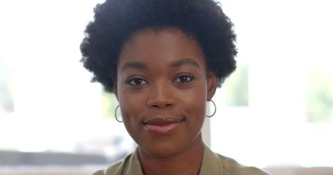 Confident Woman with Hoop Earrings Posing Against Bright Background
