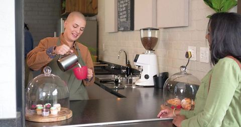 Barista pouring steamed milk into red mug serving indian customer at cozy rustic cafe