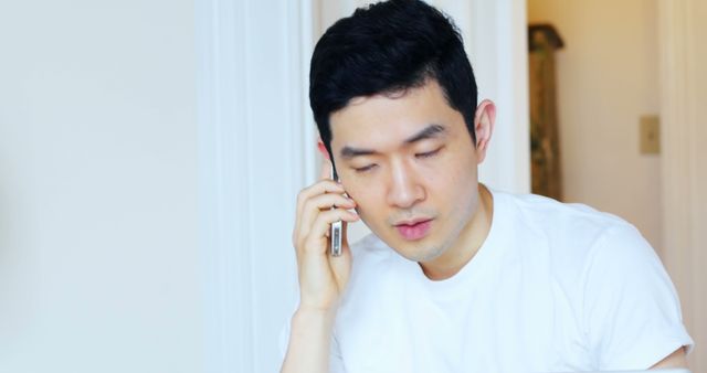 An Asian man appears engaged in a phone conversation, with copy space. His expression suggests he is listening intently or processing the information he's receiving.