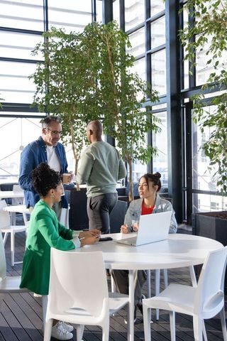 Diverse coworkers collaborating around round table in bright urban atrium with greenery