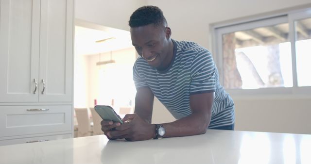 Young man smiling at smartphone in modern kitchen - Download Free Stock Images Pikwizard.com