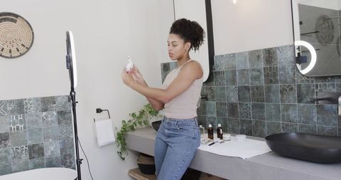 African american beauty influencer filming skincare routine with ring light at vanity