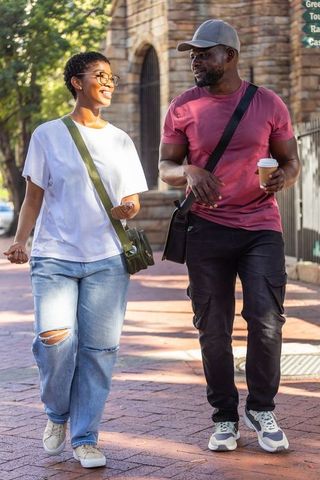 African couple walking and chatting on sunlit brick sidewalk near historic stone archway