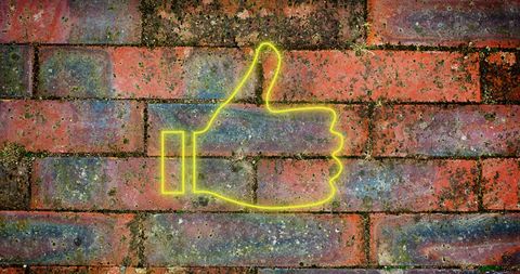 Neon thumbs up icon illuminates brick wall