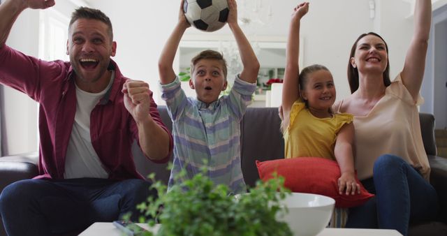 Parents and children celebrate while watching soccer in living room, conveying excitement and family bonding. Perfect for adverts on family happiness, sports enthusiasm, television promotions, or home lifestyle features.