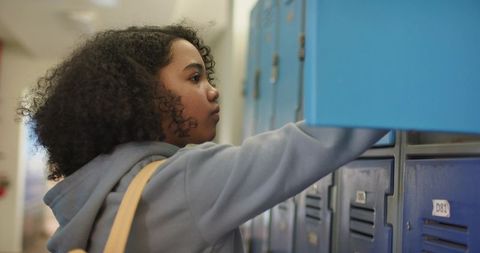 African adolescent female reaching into blue school locker wearing hoodie and backpack