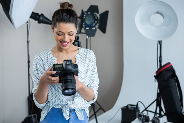 Female photographer reviewing captured photos on her digital camera in a well-equipped photography studio. Ideal for use in articles or advertisements related to photography, creative professions, studio setups, and professional equipment.