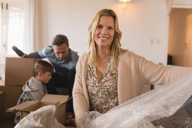 Mother smiling while family unpacks cardboard boxes in new home. Ideal for content on moving, family life, home relocation, and happiness. Perfect for real estate, moving services, and family-oriented advertisements.