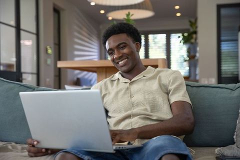 Smiling man working on laptop in modern living room with pendant lights