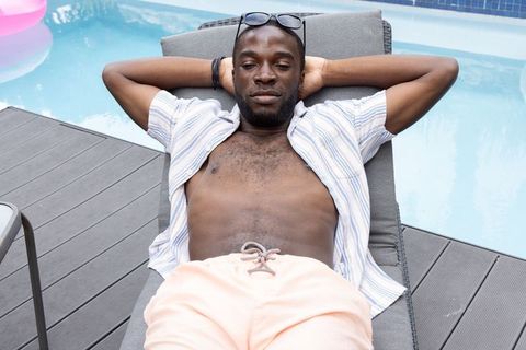 African american man lounging poolside on sun lounger wearing striped shirt and sunglasses