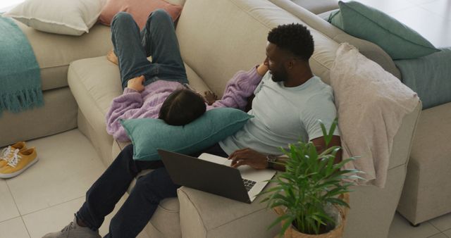 A couple relaxing on a sofa with a laptop on their lap in a cozy home living room. This can be used for themes such as home lifestyle, love, modern living, or technology use in everyday life. Ideal for blogs, websites, or magazines focusing on relationships, technology integration in homes, or relaxed, comfortable domestic settings.