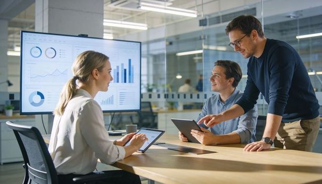 Business team collaborating over data dashboards and tablets in modern glass office