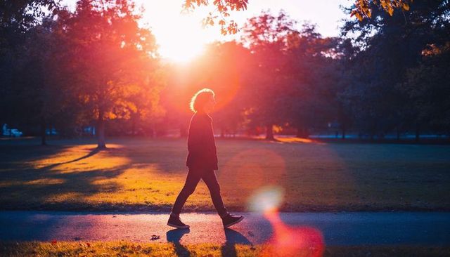 Backlit walking man at sunset with dramatic sun flare and silhouette in park