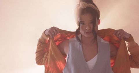 Asian woman holding orange satin jacket over shoulders posing in backlight halo headband