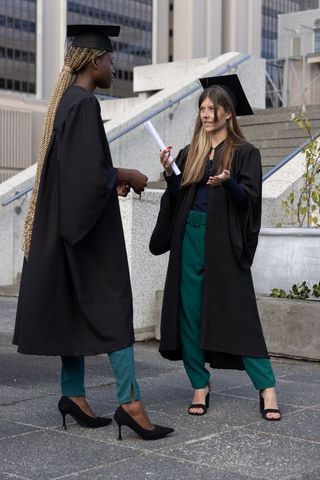 Diverse female graduates conversing on urban steps wearing caps and gowns holding diploma