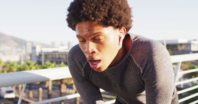 Fit african american man exercising outdoors in city, with wireless earphones, resting on footbridge. fitness and active urban outdoor lifestyle.