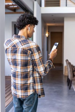 Young Man Using Smartphone with Wireless Earbuds Indoors