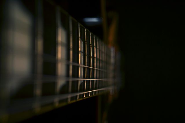 Detailed close-up showing the guitar neck and strings in dramatic lighting. Ideal for use in music-related content, promotional materials for music schools, artistic projects, or backgrounds for musical event advertisements.