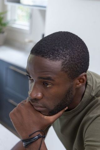Adult african american man leaning on kitchen counter, gazing thoughtfully out window