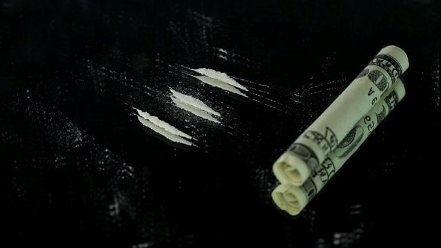 Video depicts three lines of cocaine next to a rolled dollar bill on a black surface. Represents themes of drug usage, substance abuse, and addiction. Suitable for articles or campaigns addressing the dangers of drug abuse, addiction information, or discussion about illegal substances.