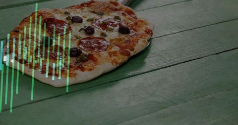 Pepperoni flatbread sitting on rustic green wooden plank with melted cheese, olives and capers