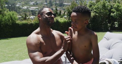 African american father bonding with son on sunny backyard lounge
