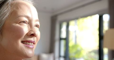 Smiling Elderly Asian Woman Enjoys Sunlight by Window