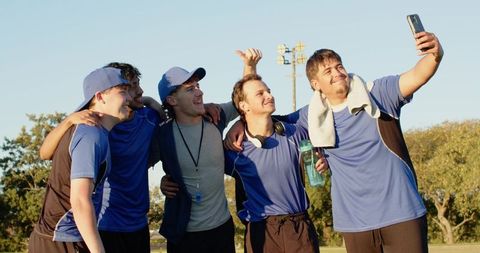 Young teammates taking selfie after game wearing blue jerseys, whistle and headphones