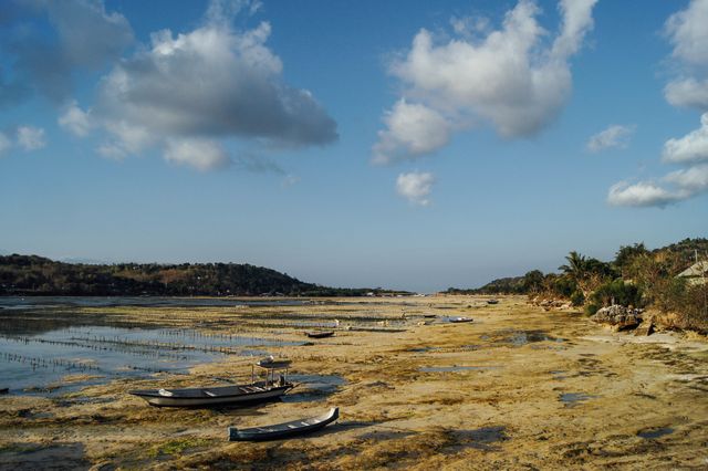 Low tide reveals coastal area with stranded fishing boats under a bright blue sky. Scenic view of seaside landscape, ideal for conveying themes of relaxation, natural beauty, and tropical island life. Useful for travel blogs, holiday brochures, nature documentaries, and relaxation-themed content.