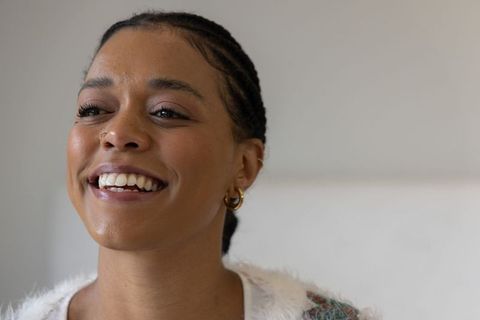 African american woman smiling and turning at home wearing knit sweater and gold hoops