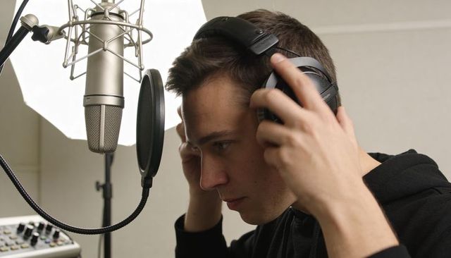 Male vocalist adjusting headphones in home studio recording with condenser microphone