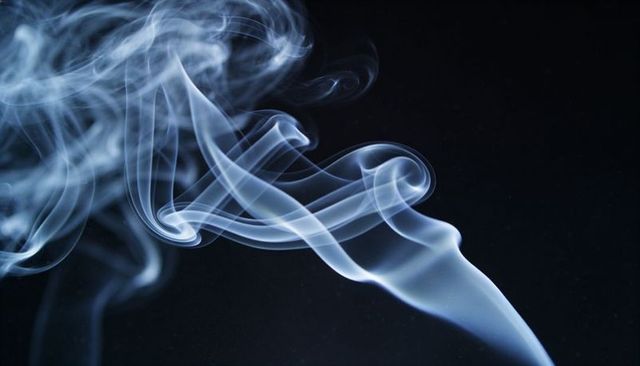 Blue smoke ribbons curling and twisting over deep black background for minimalist abstract