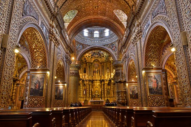 This scene captures the elaborate interior of a historic baroque cathedral, characterized by its rich golden details, ornately carved arches, and stunning painted artwork. The intricate design is covered in gold leaf, showcasing the grandeur of sacred art and architecture. Perfect for illustrating themes related to religion, history, culture, and the artistry of baroque churches. This can be used in travel brochures, historical research articles, religious educational materials, and art history presentations.