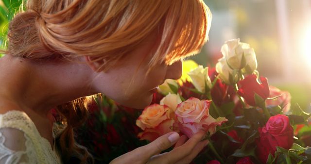 Redhead woman with strawberry blond hair enjoying the scent of vibrant blooming roses in a sunlit garden, representing beauty, tranquility, and connection with nature. Ideal for use in advertisements promoting relaxation, floral products, natural beauty campaigns, wellness brands, or romantic settings.