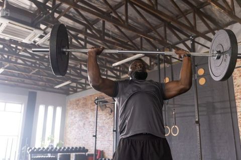 African american athlete pressing heavy barbell overhead in industrial warehouse gym