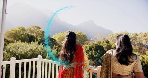 South asian women celebrating holi on balcony throwing turquoise powder toward mountains