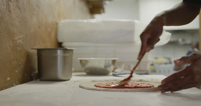 Chef spreading tomato sauce on pizza dough in restaurant kitchen - Download Free Stock Images Pikwizard.com