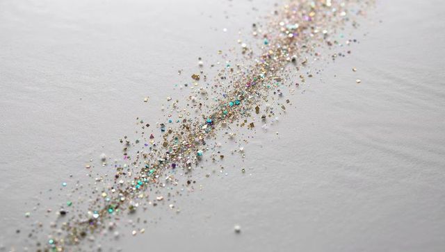 Glittering diagonal trail of iridescent gold and silver sequins on white textured paper