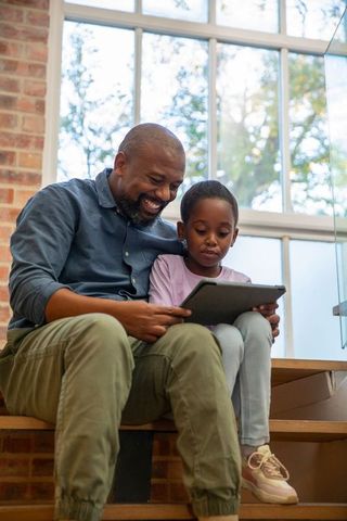 African american father and daughter sharing tablet on wooden steps, learning together