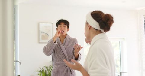 Asian couple brushing teeth together morning routine in bright minimalist bathroom
