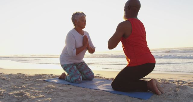 Biracial senior couple practising yoga on yoga mats at the beach. healthy outdoor leisure time by the sea.
