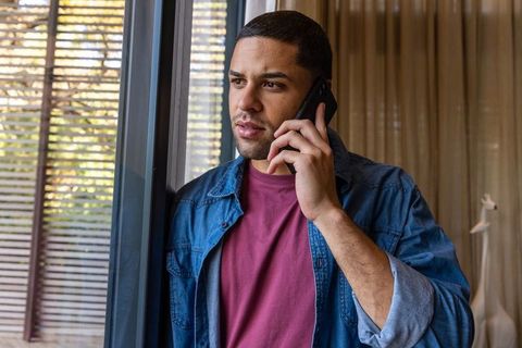 Relaxed man using smartphone by glass door at home