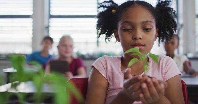 Portrait of african american schoolgirl holding small plant, looking at camera. children at primary school in summer.