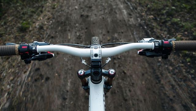 Riding mountain bike pov on singletrack forest trail with white handlebar and brown grips