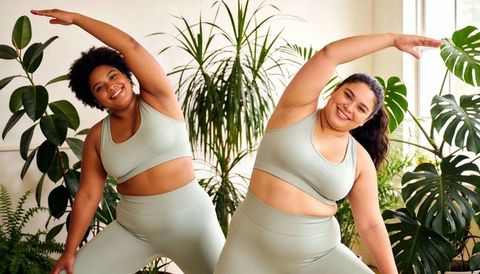Curvy duo stretching in sage activewear among indoor plants for inclusive wellness
