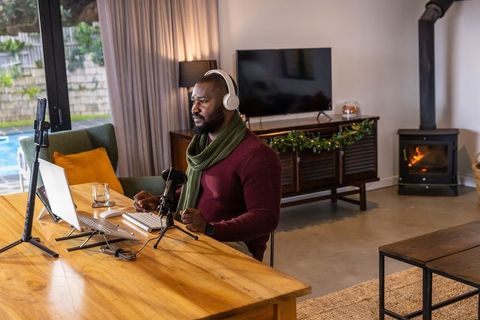 African american man recording podcast in cozy modern home studio with laptop and microphone