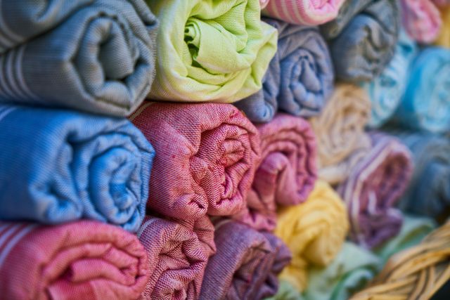 Colorful rolled fabrics are displayed, arranged in a neat stack, showcasing various vibrant colors and patterns. Ideal for use in marketing materials for fabric stores, sewing and craft projects, and online textile advertisements. Useful in blog posts about fabric selection and textile shops.