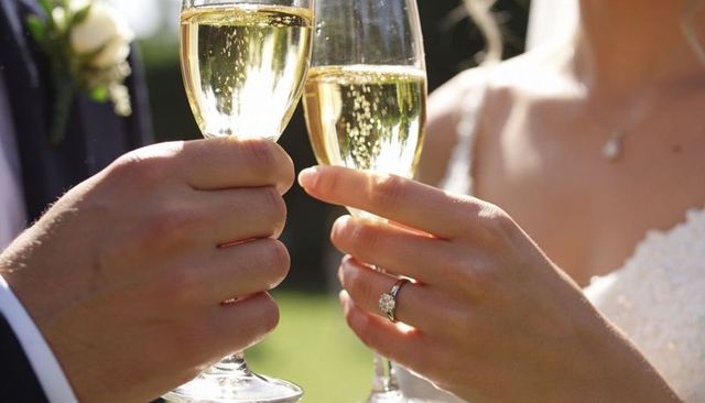 Clinking champagne flutes at wedding showing bride engagement ring and groom boutonniere